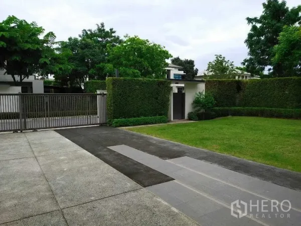 Detached House for rent or sale in Mueang Nonthaburi, Nonthaburi - Gated driveway with trimmed hedges and a spacious green front yard.