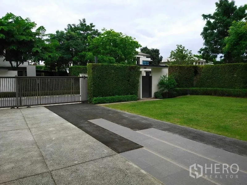 Detached House for rent or sale in Mueang Nonthaburi, Nonthaburi - Gated driveway with trimmed hedges and a spacious green front yard.