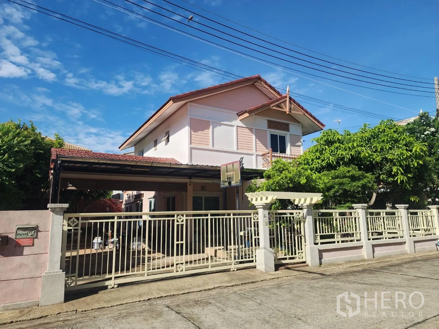 独栋房屋 for rent in Lam Luk Ka, Pathum Thani - 正面视角，带围栏的大门、带顶车棚与庭院树木。