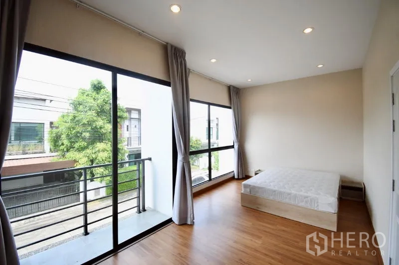 Detached House for rent in Prawet, Bangkok - Master bedroom with large corner windows, balcony access, and wood flooring.