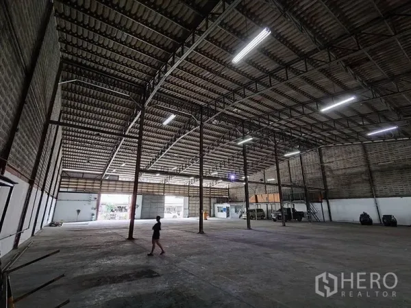 Warehouse for rent in Bang Phli, Samut Prakan - Expansive warehouse hall featuring a high truss ceiling and large shutter doors for loading.