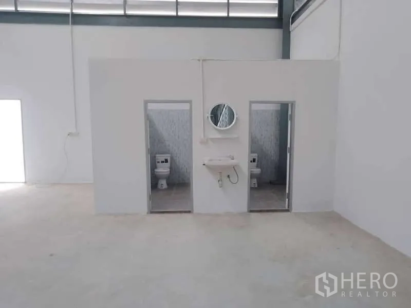 Warehouse for rent in Khlong Toei, Bangkok - Two restroom cubicles with toilets and a wall-mounted sink inside the warehouse.