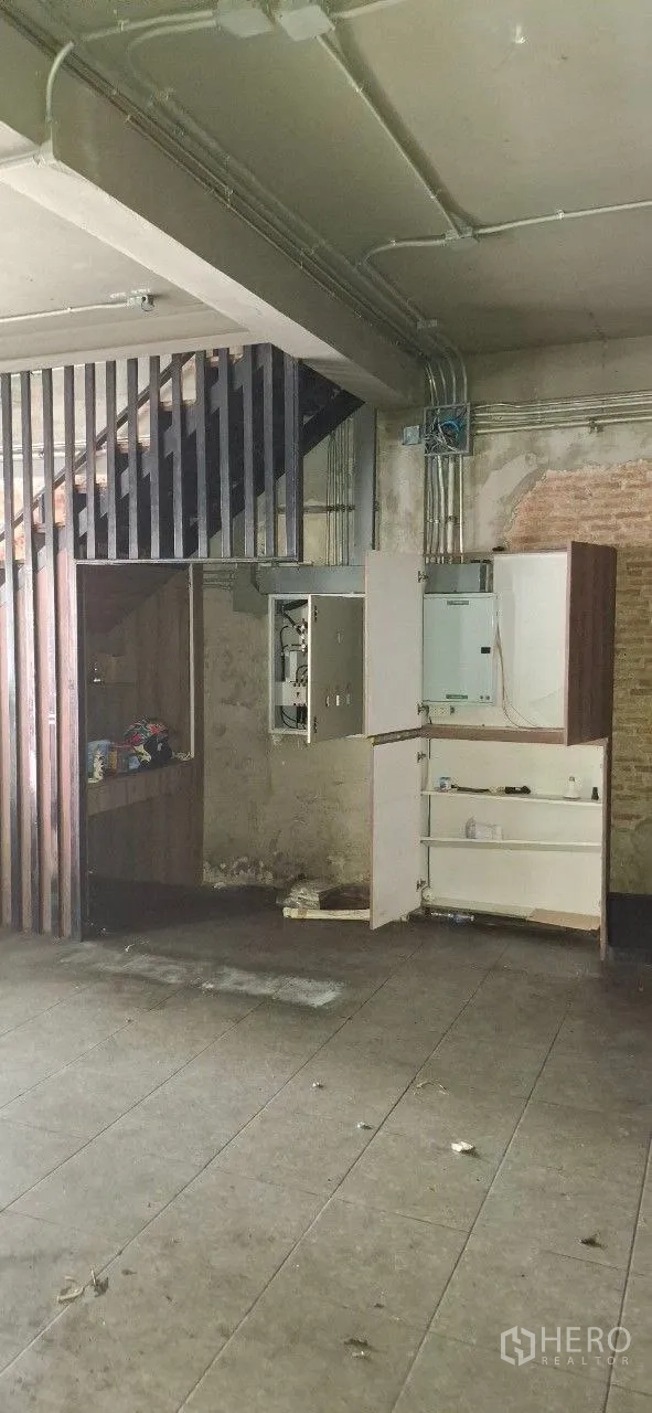 Shophouse for rent or sale in Watthana, Bangkok - Under-stair storage with open electrical cabinet, conduits, and built-in shelves in a bare space.
