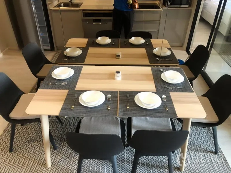 Condominium for rent in Pathum Wan, Bangkok - Six-seat dining table neatly set with tableware beside a mirrored wall.