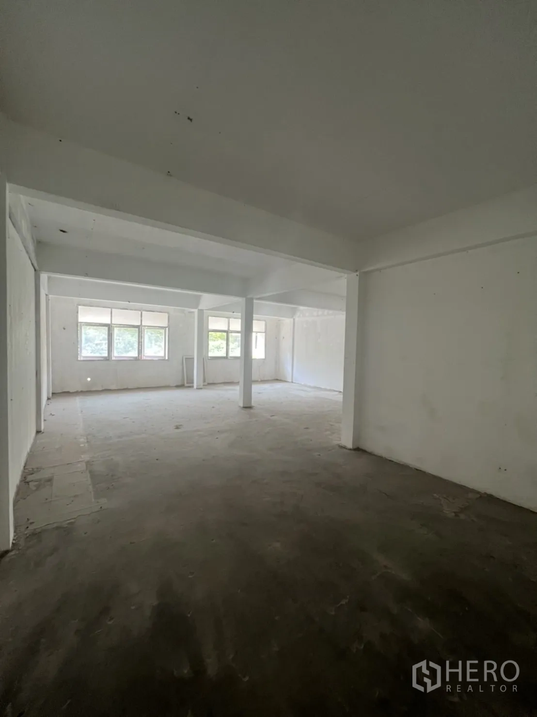 Shophouse for rent in Watthana, Bangkok - Spacious empty floor with large windows and unfinished concrete flooring.