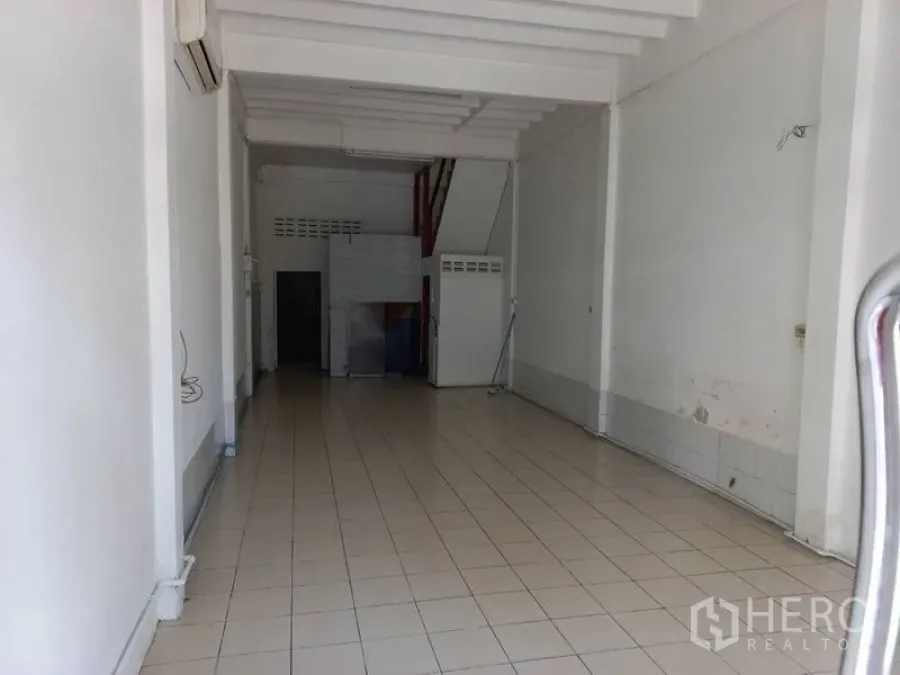 Shophouse for rent in Khlong Toei, Bangkok - Open-plan ground floor of a shophouse with white walls, tiled flooring, high ceiling beams and a rear service area with bathroom door.