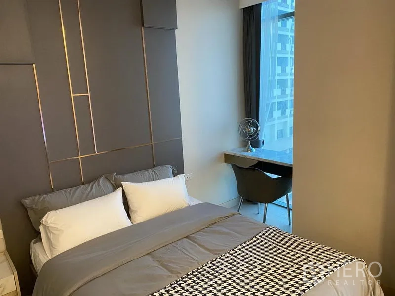 公寓 出租在Khlong Toei, Bangkok - 舒适卧室带软包背景墙、床品与窗边书桌，视野为城市景观。