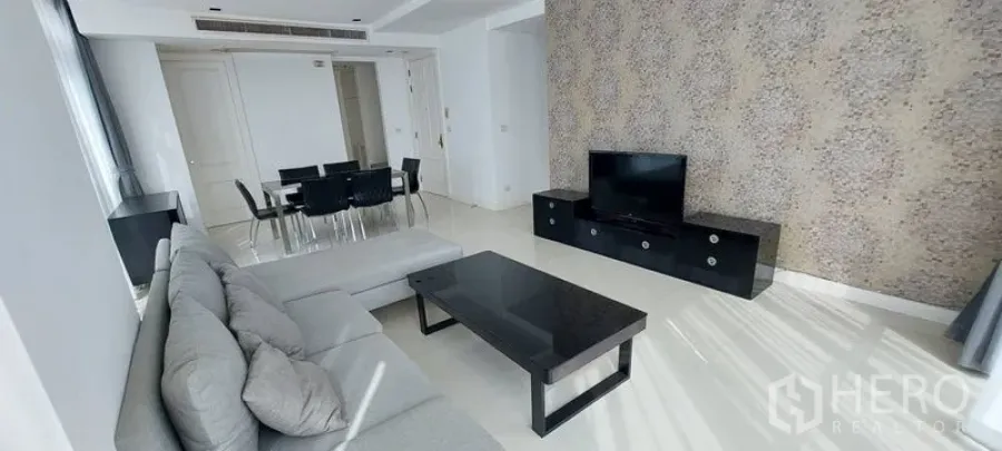 Condominium for rent in Pathum Wan, Bangkok - Living room with L-shaped gray sofa, TV console, feature wall, black coffee table and adjacent dining space.
