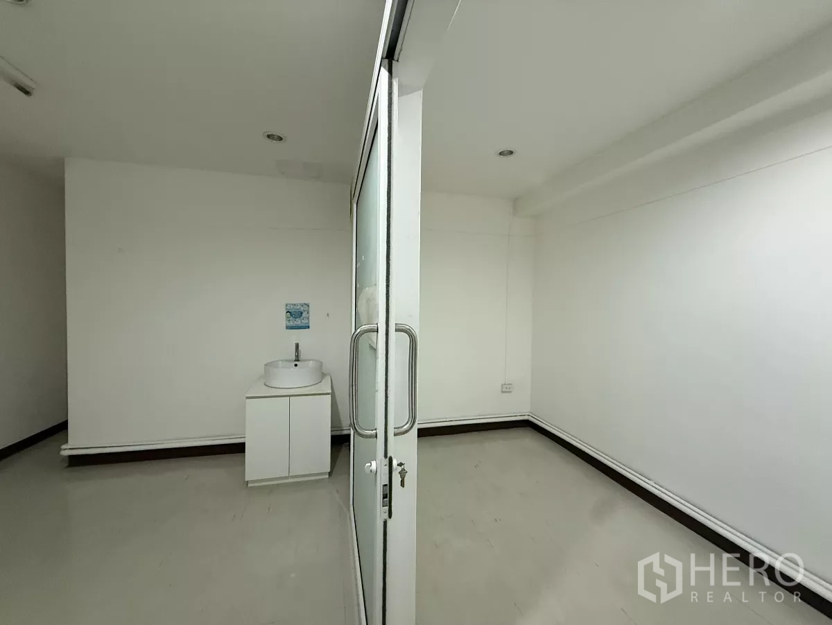 Office Space for rent in Din Daeng, Bangkok - Compact white office with sliding glass door and a vanity sink cabinet.