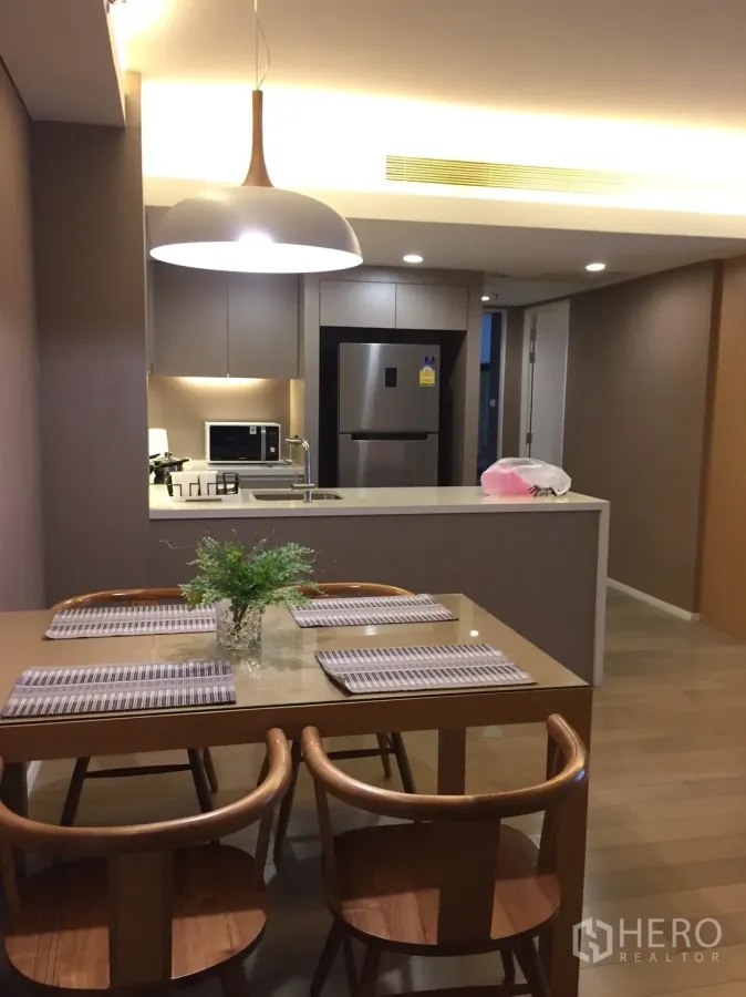 Condominium for rent in Watthana, Bangkok - Open-plan dining area with wooden table, pendant light and a view to the modern kitchen island.
