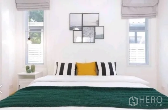 Townhouse for rent in Khlong Toei, Bangkok - Minimalist bedroom with white walls, framed art, and two narrow windows flanking the bed.