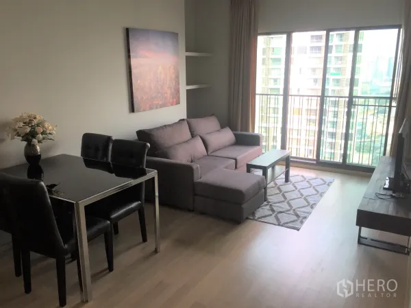 Condominium for rent in Bangkok - Bright living room with floor-to-ceiling windows, city-view balcony, sectional sofa, rug, and TV stand.
