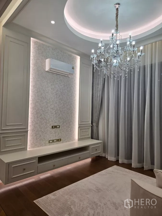 Detached House for rent or sale in Bang Kapi, Bangkok - Sitting room with chandelier and floating TV cabinet framed by tall curtains.