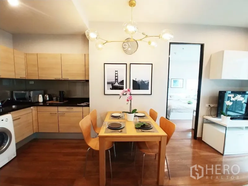 Condominium for rent in Pathum Wan, Bangkok - Open kitchen with wood cabinets, dining table for four, modern chandelier and in-unit washing machine.