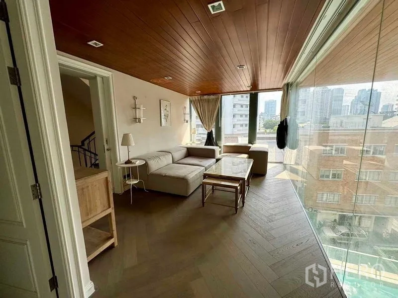 Townhouse for rent in Watthana, Bangkok - Glass-walled living area with city views and L-shaped sofa.