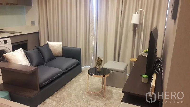 Condominium for rent in Khlong Toei, Bangkok - Cozy living room with sofa, round coffee table, floor lamp, and curtains