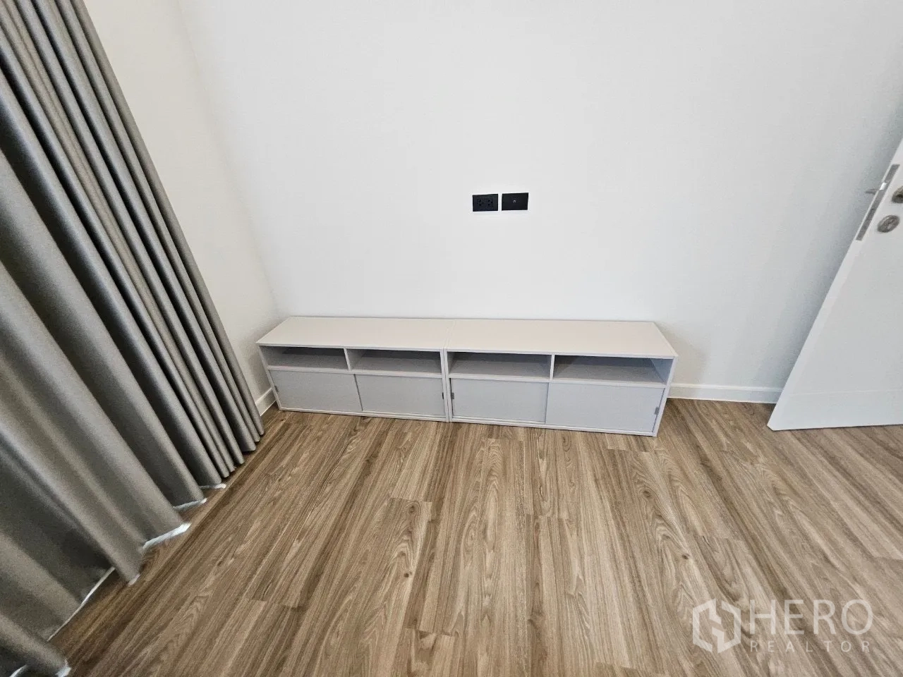 Detached House for rent in Bang Kapi, Bangkok - Compact bedroom wall with low white TV cabinet and grey curtains.