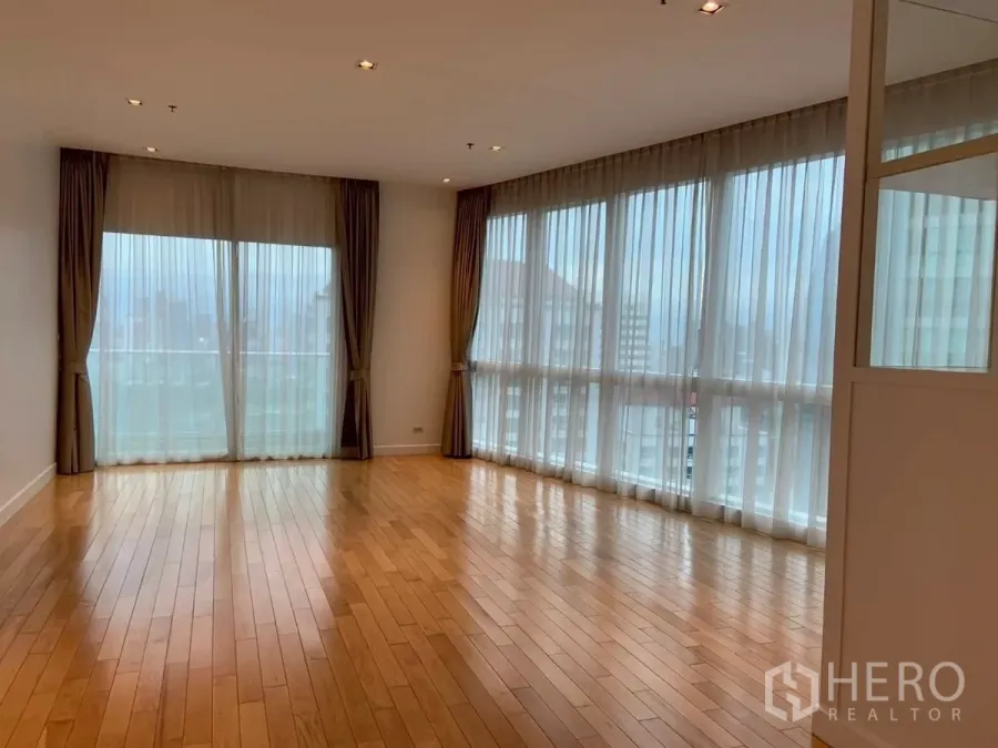 Condominium for rent in Khlong Toei, Bangkok - Bright corner living room with floor-to-ceiling windows, sheer curtains and hardwood flooring.