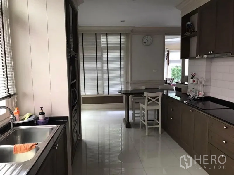 Detached House for rent in Bang Khen, Bangkok - Open-plan kitchen with black stone countertops, sink and windows with blinds.