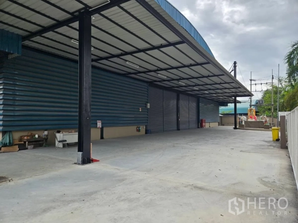 Factory for rent in Si Racha, Chon Buri - Covered loading bay with metal roof, multiple roller shutter doors and a wide concrete yard for trucks.