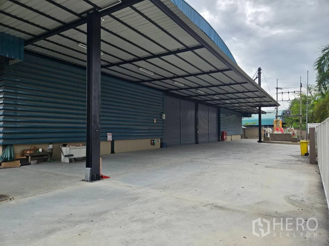 Factory for rent in Si Racha, Chon Buri - Covered loading bay with metal roof, multiple roller shutter doors and a wide concrete yard for trucks.
