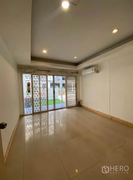 Townhouse for rent in Khlong Toei, Bangkok - Ground-floor room with large glass doors and security grilles opening to the garden.