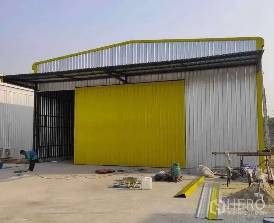 Warehouse for rent in Khlong Sam Wa, Bangkok - Metal-clad warehouse with bright yellow sliding door and loading canopy on a concrete yard in Khlong Sam Wa, Bangkok.