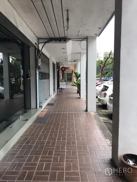 Retail Space for rent in Khlong Toei, Bangkok - Covered sidewalk arcade with shopfronts, tiled walkway and parking bays outside, suitable for steady foot traffic.