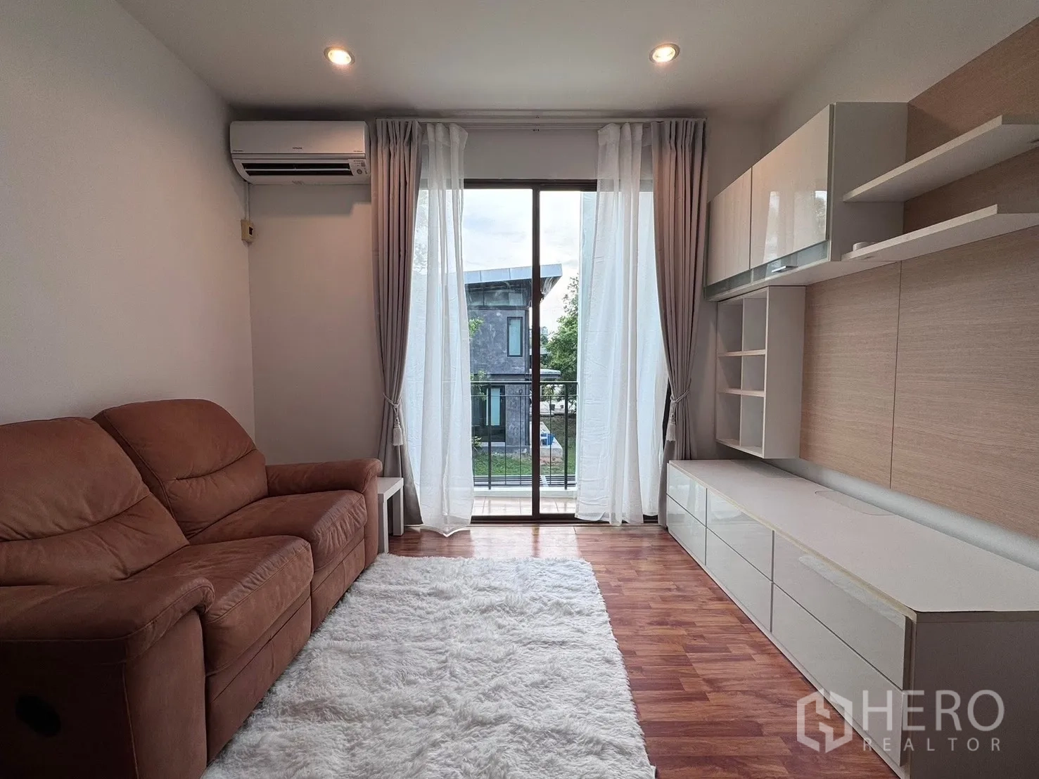 Townhouse for rent in Phra Khanong, Bangkok - Living room with built-in TV cabinet and curtains beside the balcony.