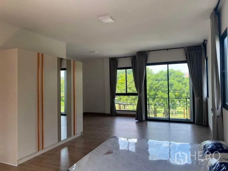 Detached House for rent in Khan Na Yao, Bangkok - Spacious master bedroom with wardrobes, wood flooring and wide park‑view windows.