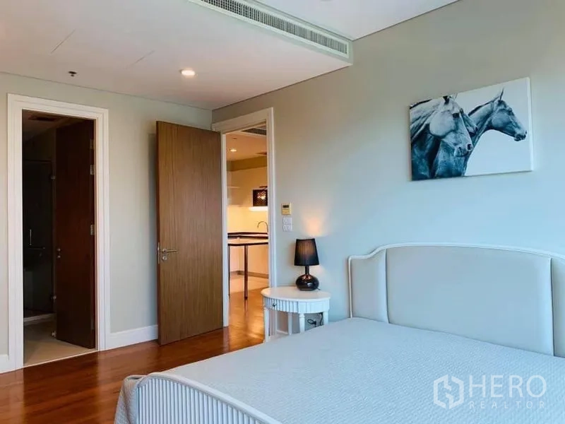 Condominium for rent in Khlong Toei, Bangkok - Cozy bedroom with upholstered bed, bedside table and doorway to the ensuite bathroom.