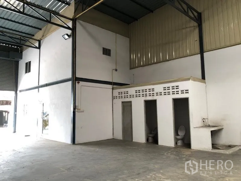 Warehouse for rent in Pak Kret, Nonthaburi - Corner of the warehouse showing built-in restrooms, a sink, and exposed steel truss roof.