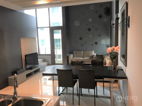 Condominium for rent in Khlong Toei, Bangkok - Bright living and dining space with floor-to-ceiling windows, balcony door, feature wall and flat-screen TV.