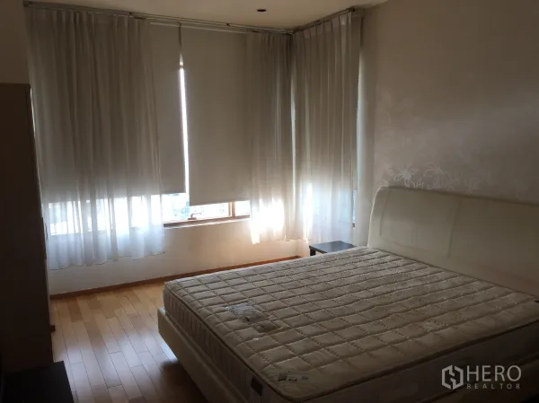 Condominium for rent or sale in Khlong Toei, Bangkok - Master bedroom with king-size bed, wood flooring, and wraparound windows with blinds and sheer curtains.