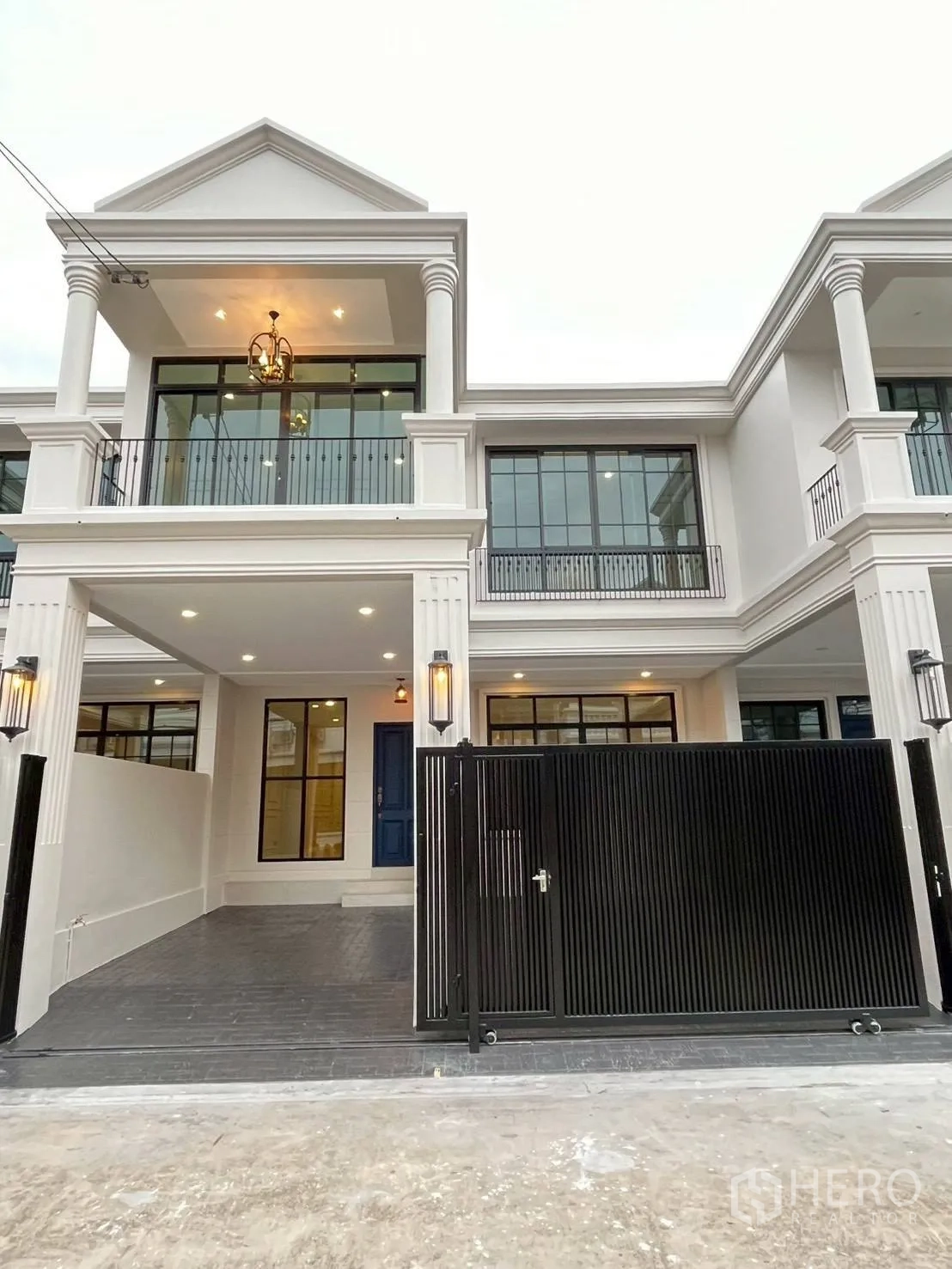 联排别墅 for rent in Khlong Toei, Bangkok - 白色典雅外立面的联排别墅，带阳台与暖色照明及黑色滑动大门。