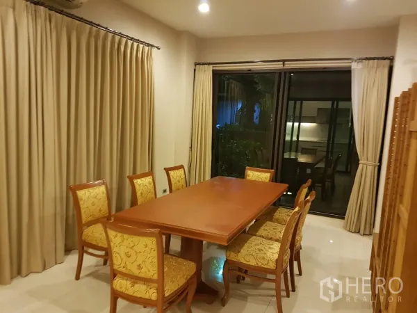 Townhouse for rent in Bang Kapi, Bangkok - Dining area with wooden table for eight, upholstered chairs and floor-to-ceiling curtains.