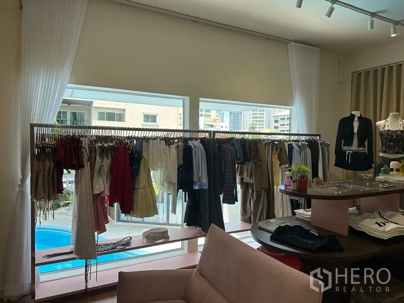 零售空间 for rent in Khlong Toei, Bangkok - 大窗前的衣架陈列，窗外可见泳池与粉色低矮展示架。