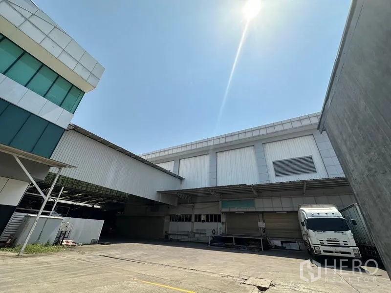 Warehouse for rent in Lam Luk Ka, Pathum Thani - Driveway leading to a covered loading area with warehouse walls and a truck front visible.