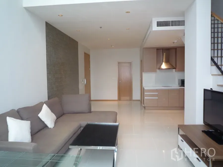 Condominium for rent in Khlong Toei, Bangkok - Duplex condo living room with sofa, TV, open kitchen and staircase in Khlong Toei, Bangkok.