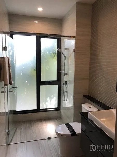Detached House for sale in Bang Kapi, Bangkok - Contemporary bathroom with glass-enclosed shower, frosted windows, vanity and toilet.