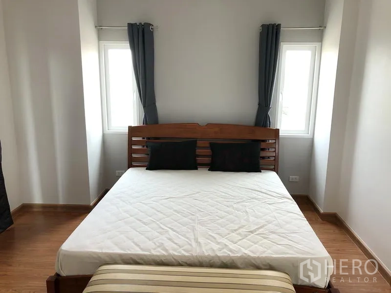 独立式住宅 出租或出售在Huai Khwang, Bangkok - 转角卧室，木床架，双侧窗户与素色窗帘
