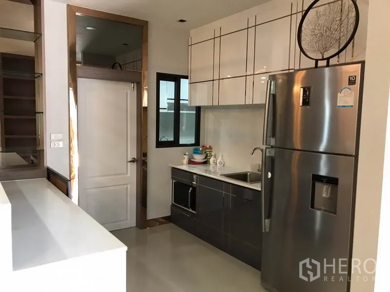 独立式住宅 出租在Bang Phli, Samut Prakan - 紧凑厨房，亮面橱柜、水槽、微波炉和双开门冰箱。