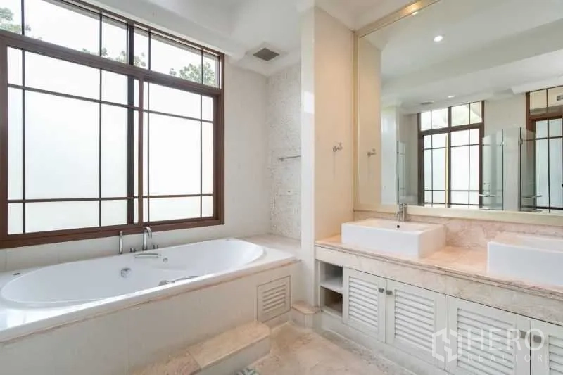 Detached House for rent in Watthana, Bangkok - Bathroom with bathtub, double vanity and oversized mirror with frosted windows.