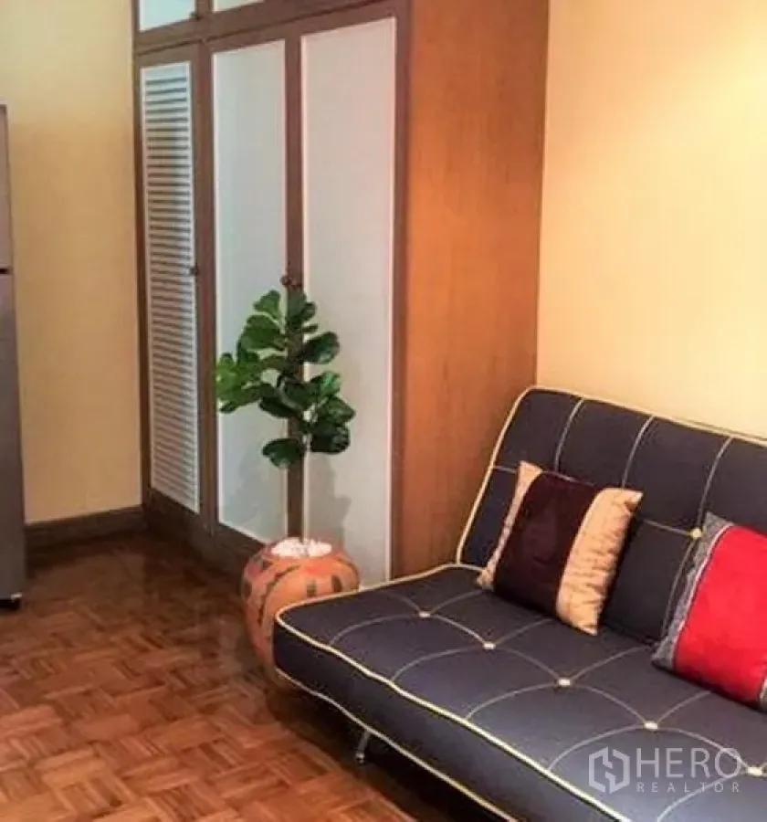 Condominium for rent in Sathon, Bangkok - Lounge corner with navy sofa and colorful cushions beside a wardrobe, refrigerator and potted plant.