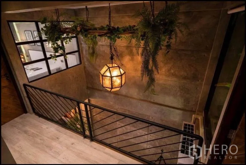 Townhouse for rent in Khlong Toei, Bangkok - Stairwell with metal railing, statement pendant lamp and hanging greenery, industrial style.