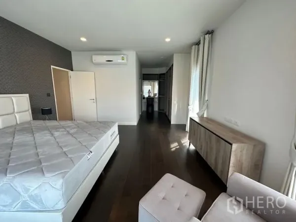 Detached House for rent or sale in Lam Luk Ka, Pathum Thani - Spacious master bedroom with wood floors, white bed, air conditioner and walk-in closet access.