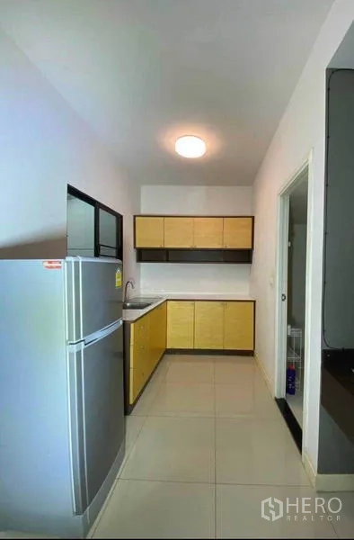 Townhouse for rent in Suan Luang, Bangkok - Galley kitchen with light wood cabinets, sink, tiled floor and refrigerator.