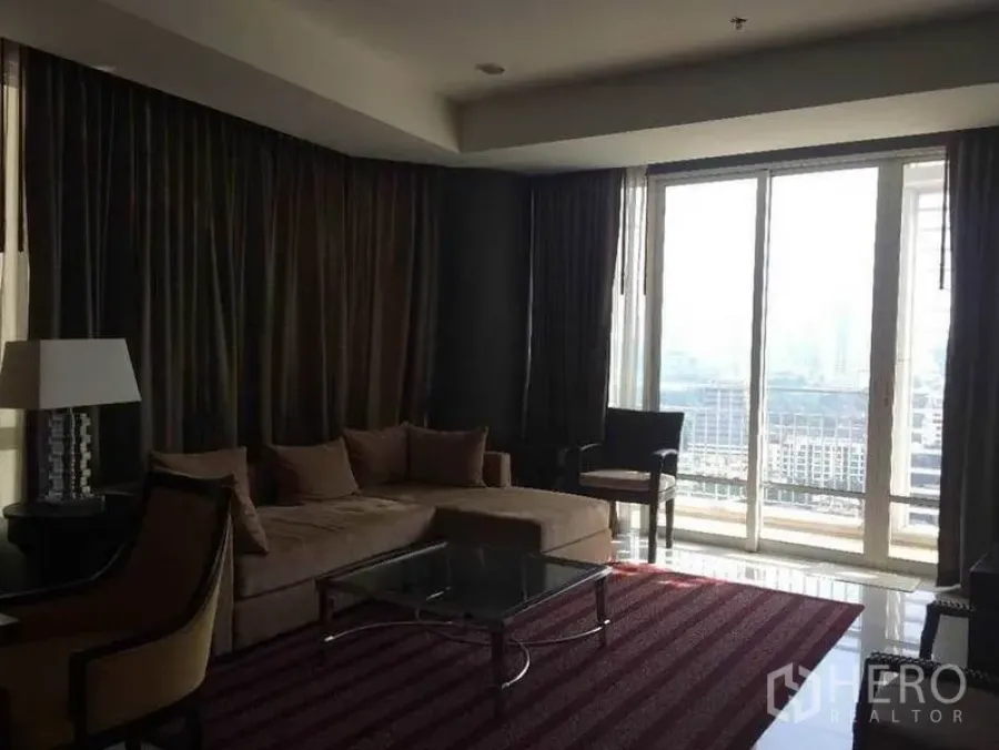 Condominium for sale in Pathum Wan, Bangkok - Lounge with sectional sofa, glass coffee table and floor-to-ceiling windows.