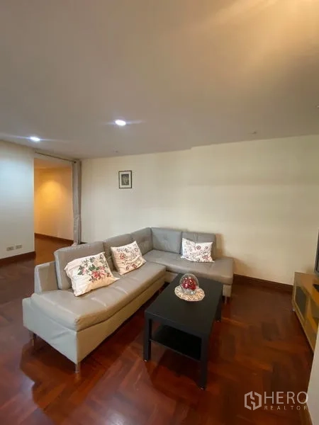 Condominium for rent in Pathum Wan, Bangkok - Cozy living room featuring an L-shaped sofa, coffee table, and TV unit on parquet flooring.