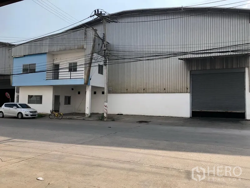 Factory for rent in Wang Noi, Phra Nakhon Si Ayutthaya - Street view of a large metal factory warehouse with a two‑storey office block and a wide roller shutter entrance.